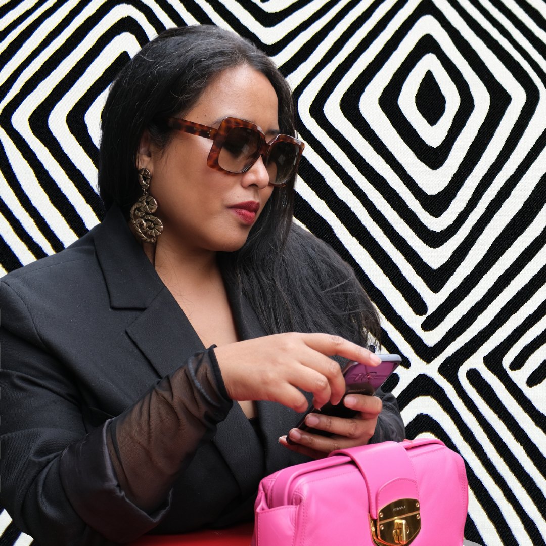 Bako Rambini checking her phone with a pink handbag